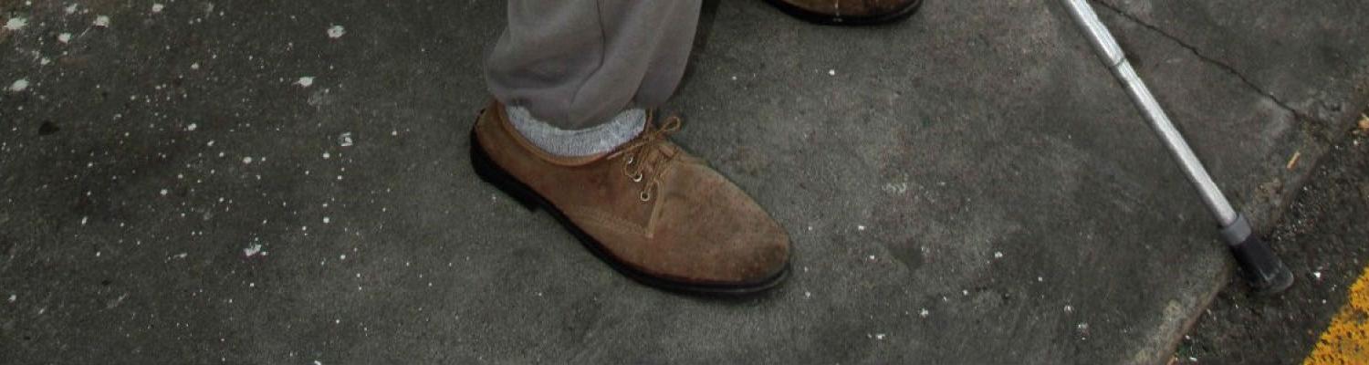 Photo of mans shoes next to his cane. 